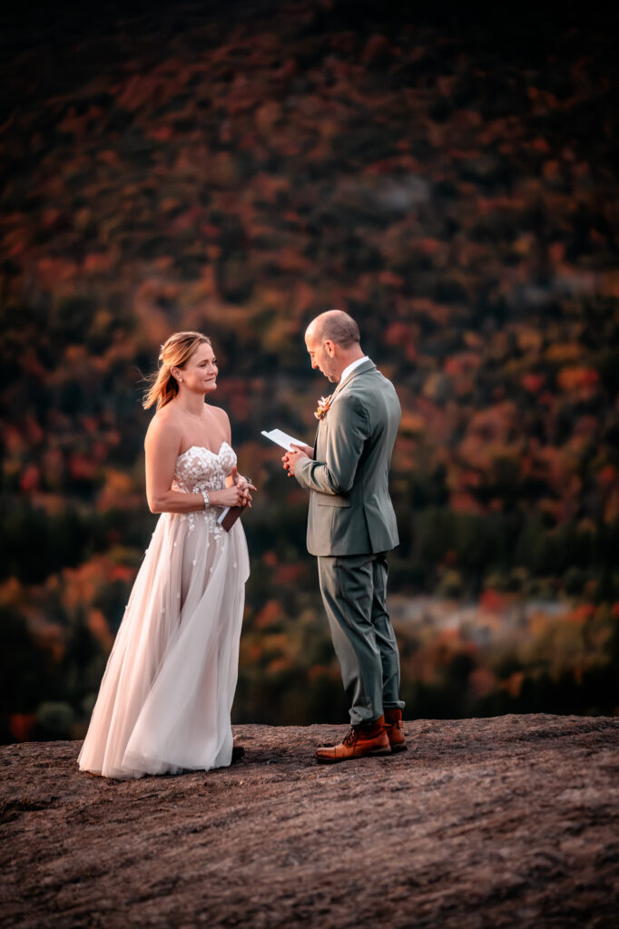 Groom reads vows to bride on the mountain with fall foliage.