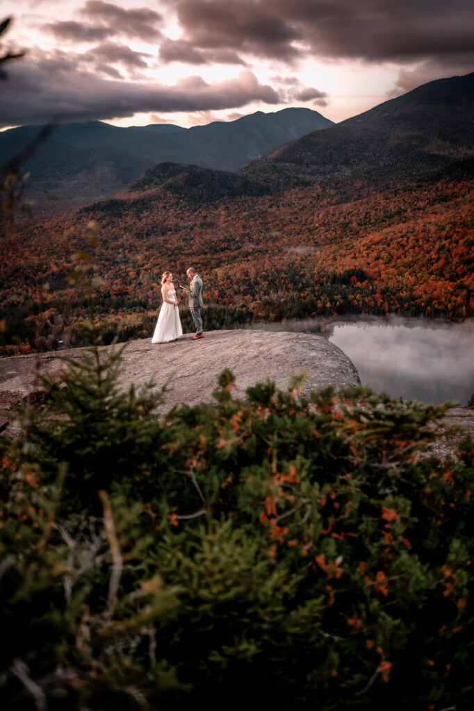 large picturesque image of bride and groom sharing vows on a mountain rock face in fall.