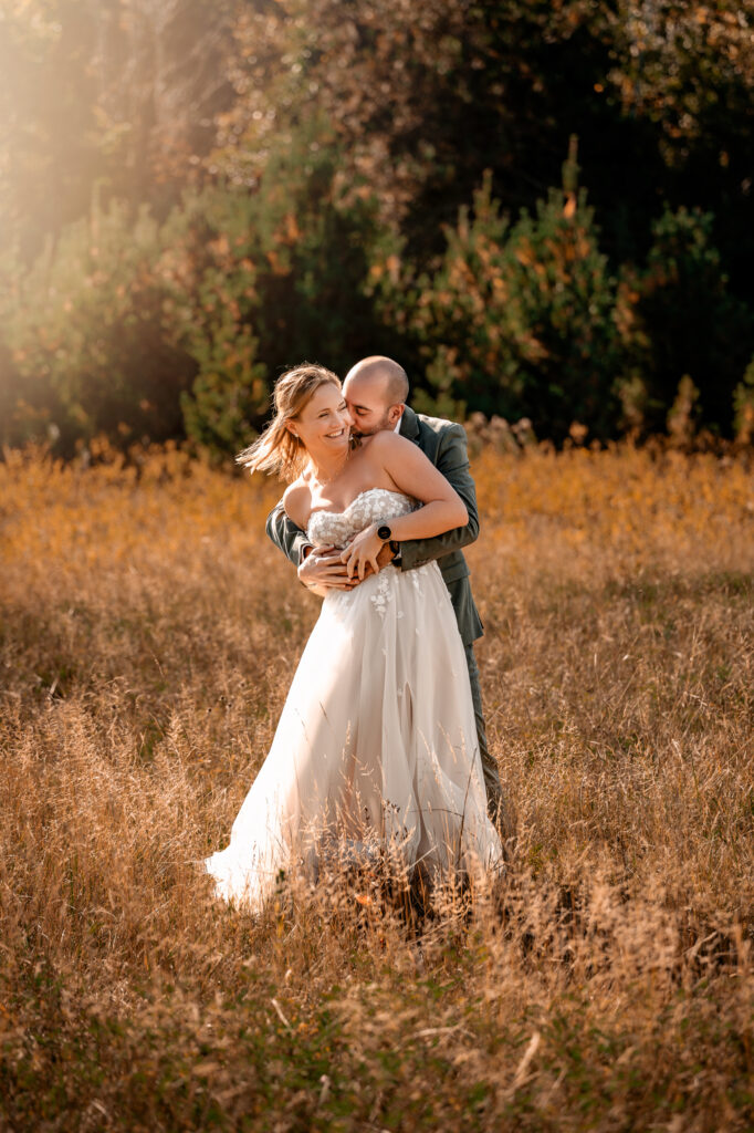 bride and groom tickle fight in a field with golden morning light