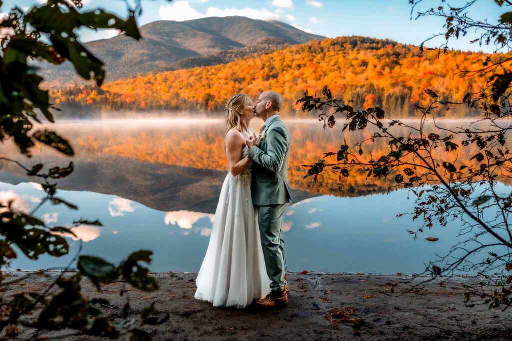 bride and groom share kiss during first dance in front of fall foliage mountains on a lake