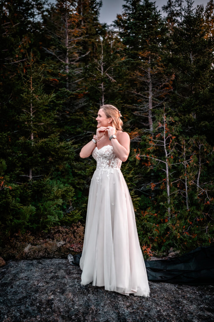 Bride puts earrings in with pine trees in the background.