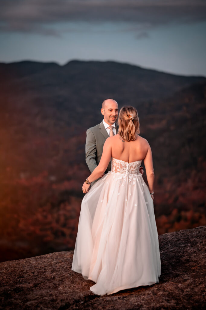 Groom sees bride for the first time at sunrise on top of a mountain in fall.