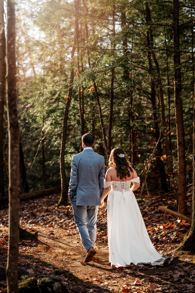 Couple walking through the sunlit forest holding hands, in a crowd free place to elope in the adirondacks