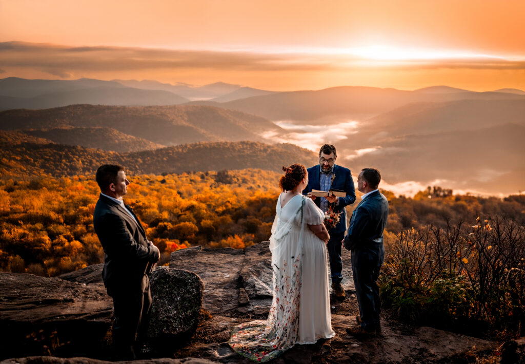 Couple exchanges vows with an officiant and witness overlooking fall colored mountains.