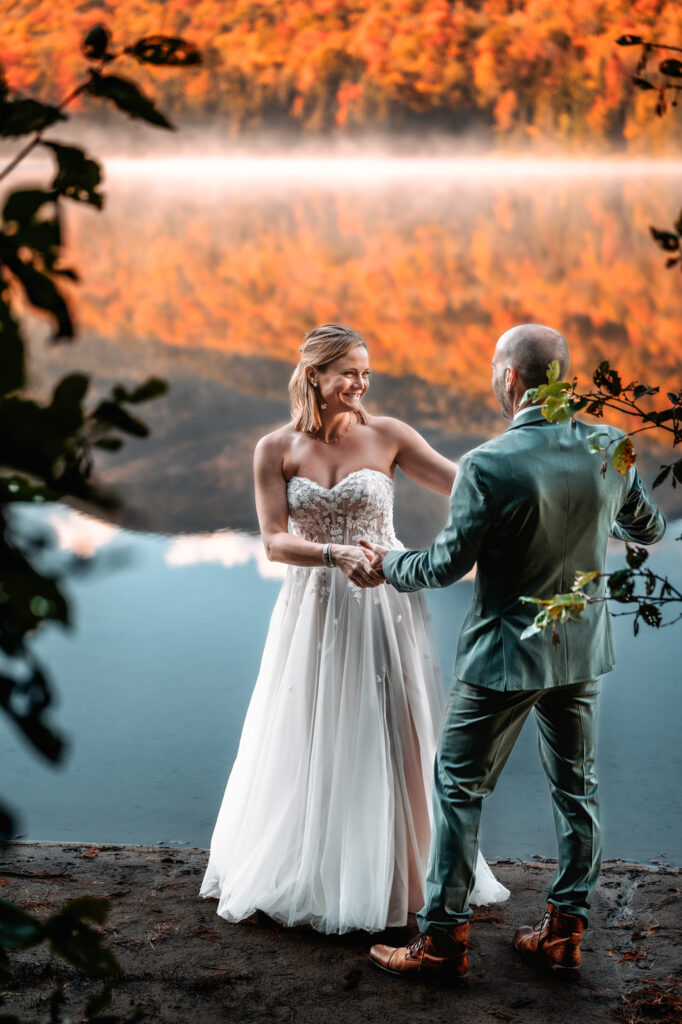 bride and groom share first dance in front of fall foliage mountains on a lake