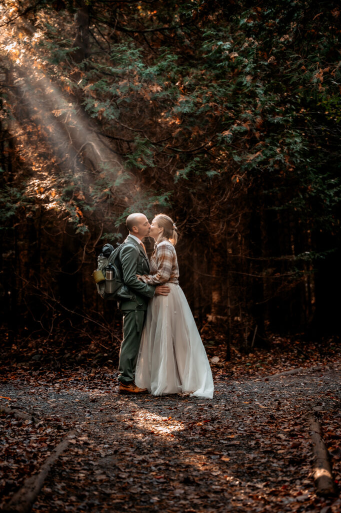 Bride kisses groom with sunrays peeking through the forest