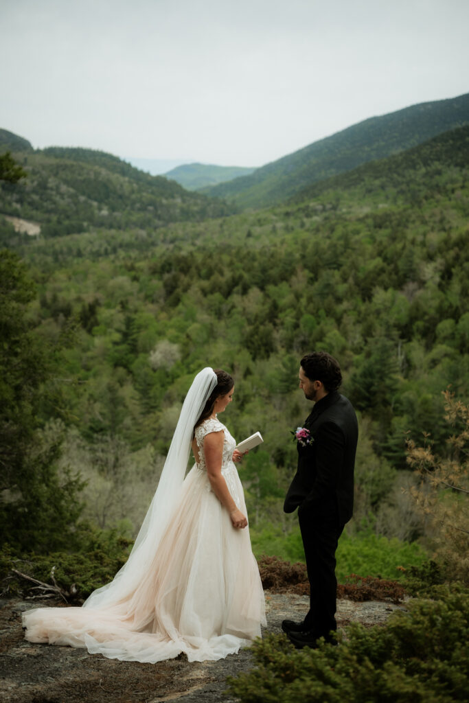 A couple exchanges vows on a mountain overlook for their elopement with green mountains behind them. 