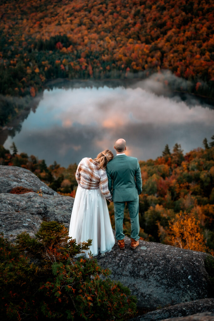 A couple who just got married overlooking the reflection of a fall sunrise with pink clouds in the sky on heart lake.
