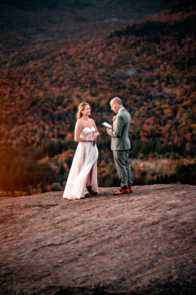 A couple exchanges vows on a mountain ledge during fall at sunrise.