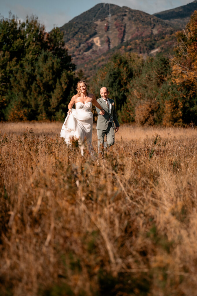 A couple shows how fun eloping can be in the adirondacks by running with each other in a field in the fall in front of whiteface mountain.