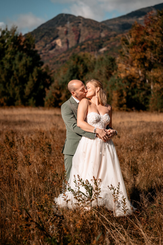 A couple kisses in a field during fall in front of whiteface mountain after getting married.
