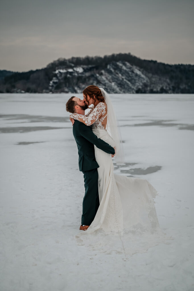 A couple kisses on a frozen lake after just getting married. 