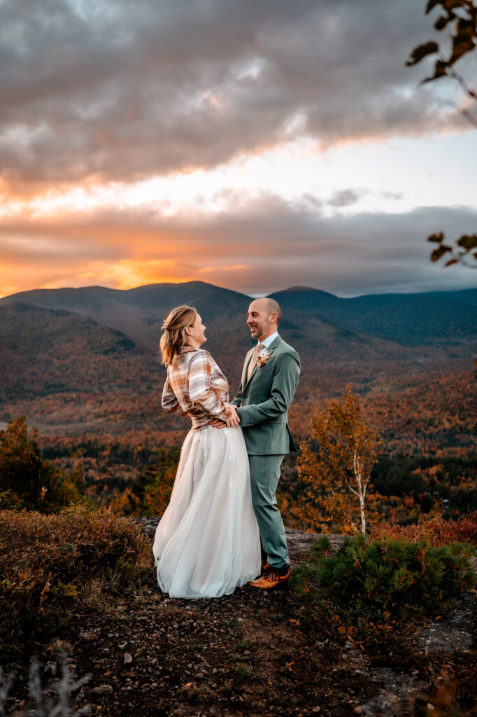 A couple who just got married tickles eachother on a peak of mount jo in the Adirondacks during the fall.