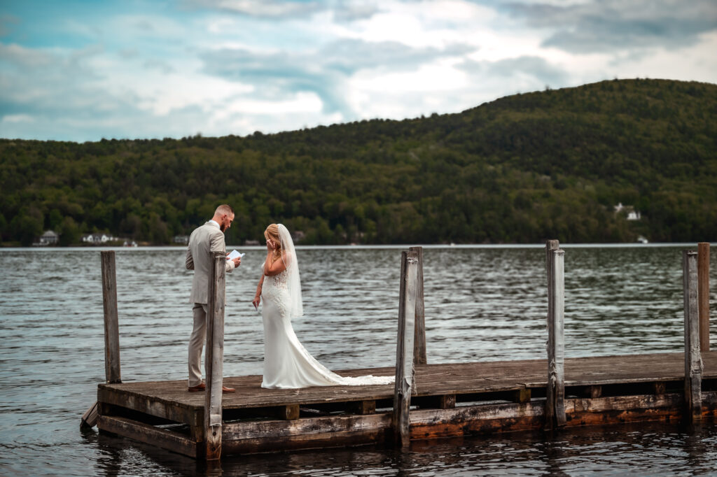 A couple on a dock who are reading vows to eachother in lake george.