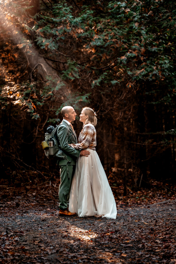 A couple that just got married looks at eachother with the light shining through the forrest onto them. 