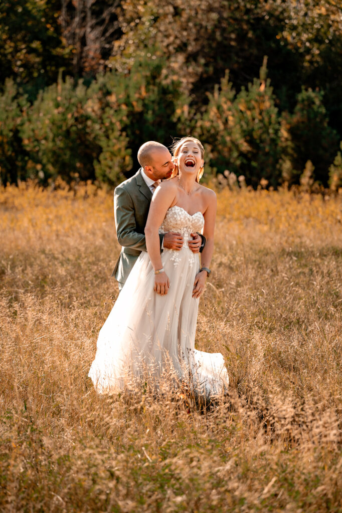 A couple has fun loving on each other giving each other kisses and running with each other in a field in the fall in front of whiteface mountain.