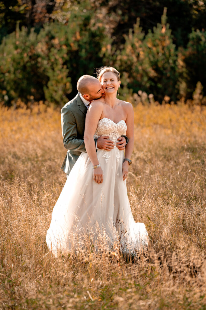 A couple has fun loving on each other giving each other kisses and running with each other in a field in the fall in front of whiteface mountain.