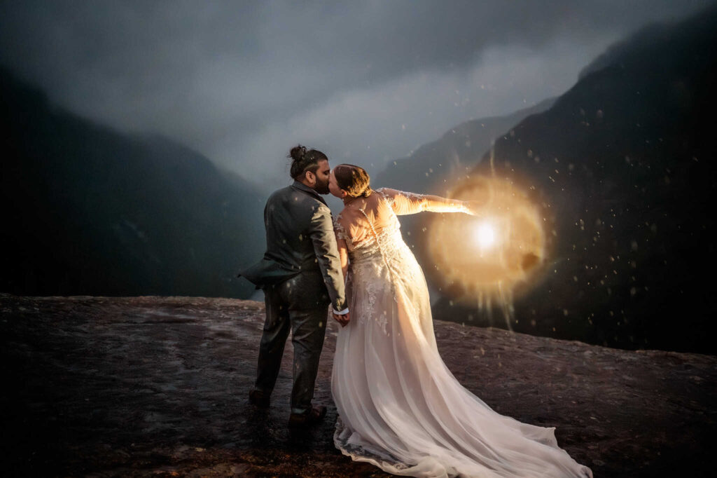 A couple has a rainy summer elopement on indian head mountain kissing with a lantern on the ledge.