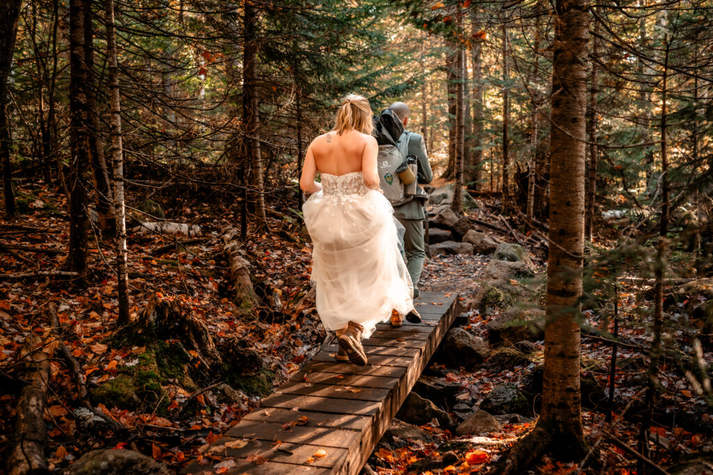 Couple elopes over a bridge over a stream in the fall in the forest in the adirondack mountains.