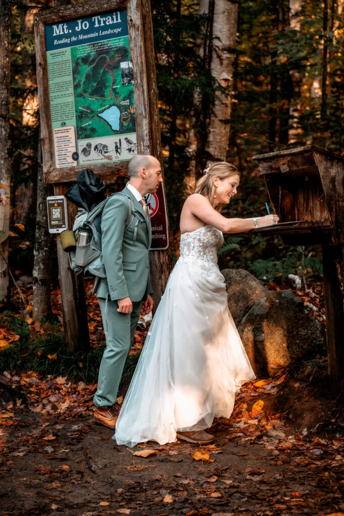 A couple who is doing a hiking elopement signs hiking log book trail register. 