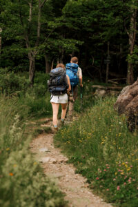 A couple walking on a trail in the adirondacks with flowers all around them.