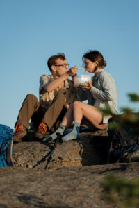 A couple eats ramen noodles at the top of a mountain in the Adirondacks.