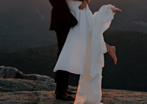 A picture of a brides feet in the air and the grooms feet with just socks on standing on a rock face in the adirondack mountains at sunset.
