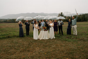 Two brides celebrate with their family after saying I Do with a toast of champagne in a misty rainy field with a mountain backdrop in the Adirondacks.