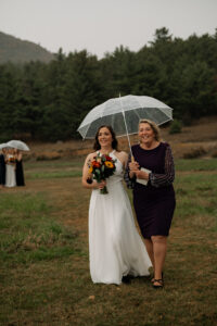A bride walks with her mother down the isle in the rain with a clear umbrella.