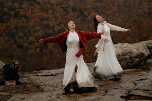 Two brides catching rain on their tongues at the top of a mountain summit.