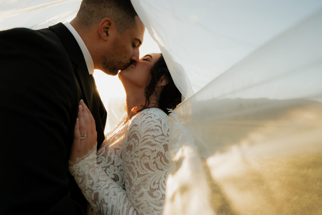 Couple kissing under veil at sunset