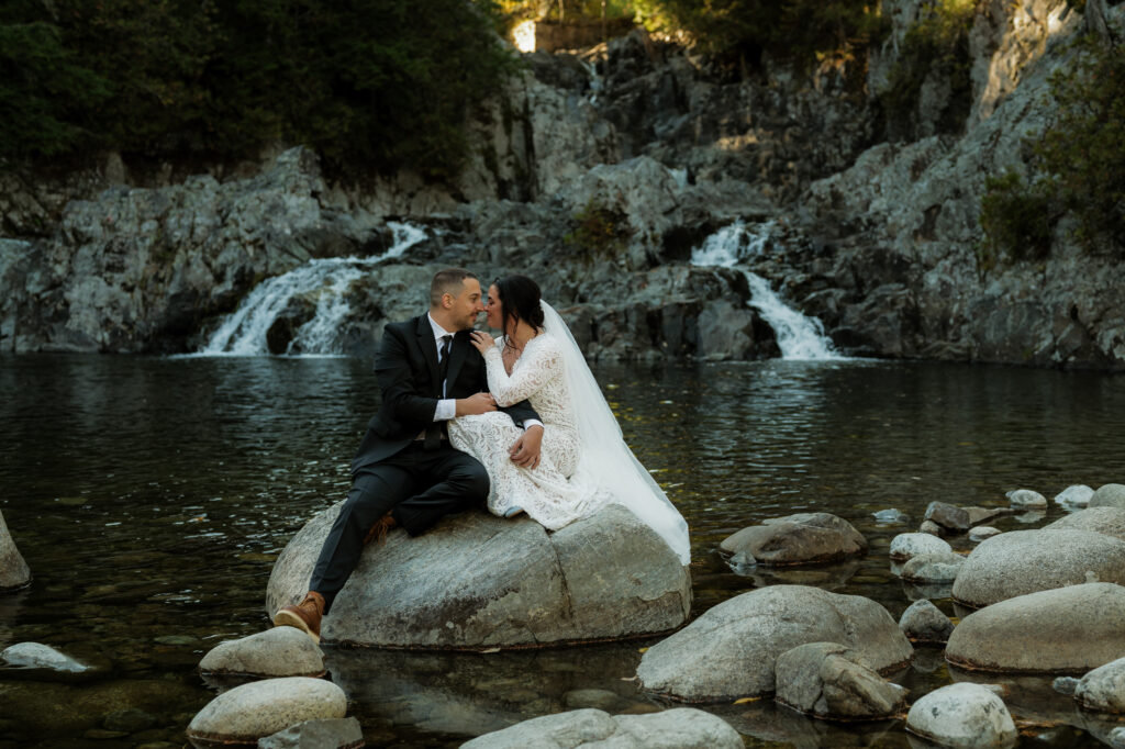Couple sits on rock at base of waterfall in the adirondacks