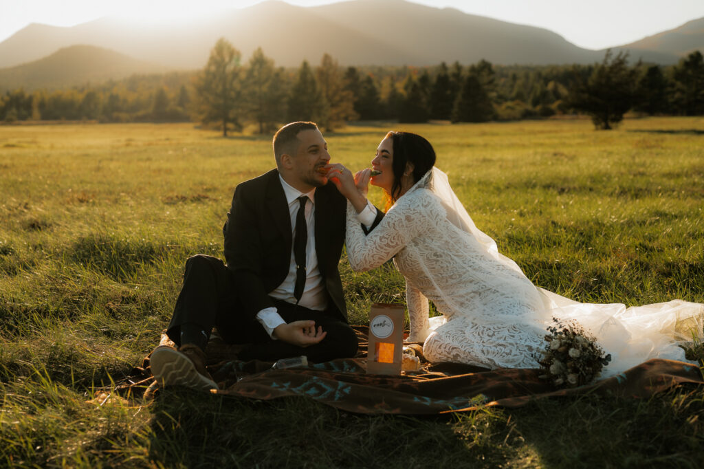 Couple eats cake together at picnic in a field in elopement day attire
