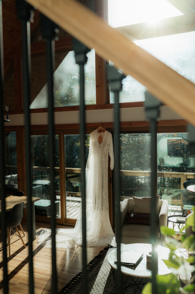 A wedding dress hanging from an a frame cabin with sun peaking in.