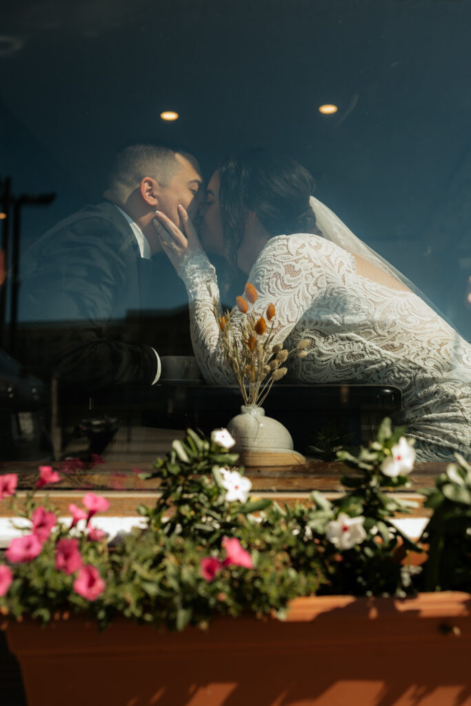 Eloping couple kisses in storefront window at coffee shop in the adirondacks
