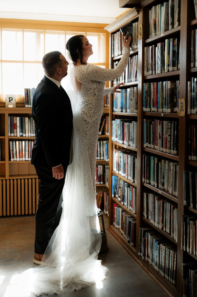 Eloping couple picks out a book off of a book shelf in a library.