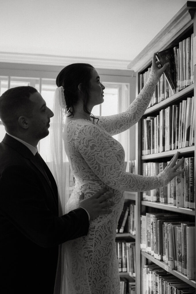 Eloping couple picks out a book off of a book shelf in a library.