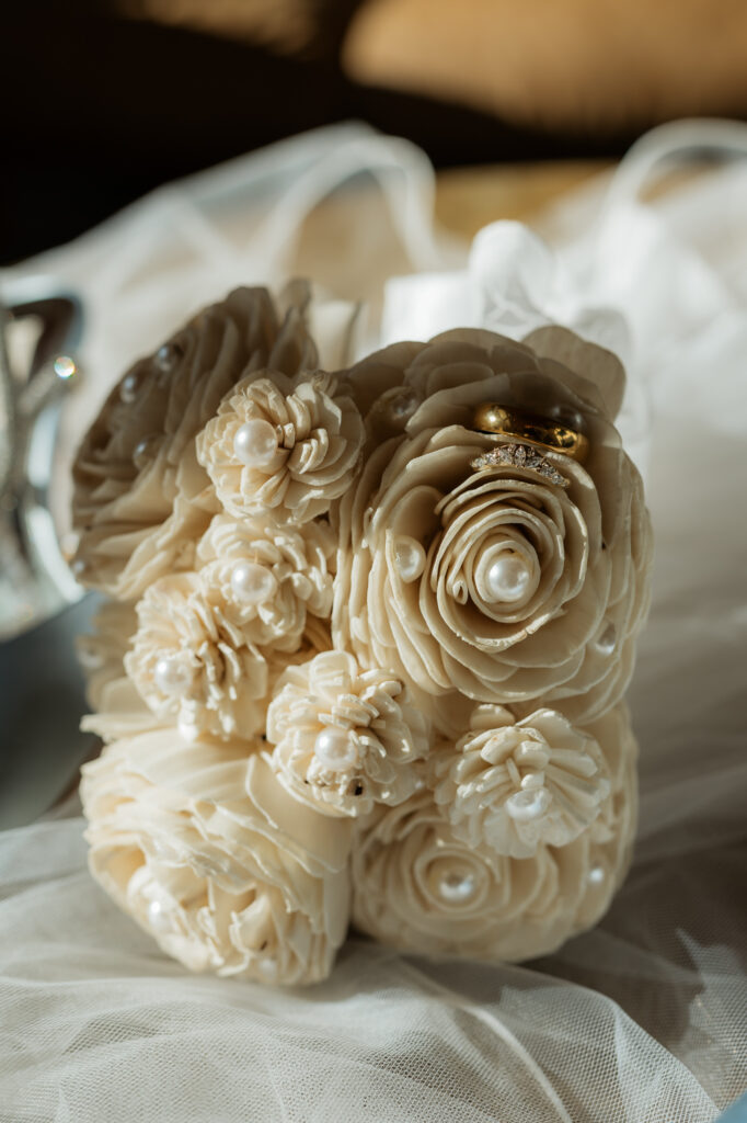 Wedding rings on a bouquet of fake florals on a veil with sun peaking in.