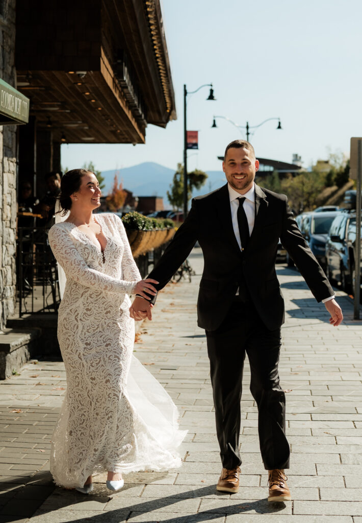 Bride and groom hold hands walking through lake placid New York in the Adirondacks.