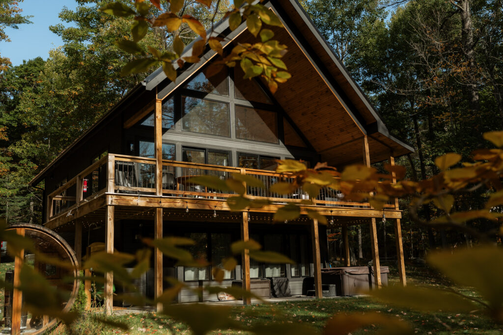 An adirondack cabin with sun hitting it as seen peaking through fall leaves in a tree.