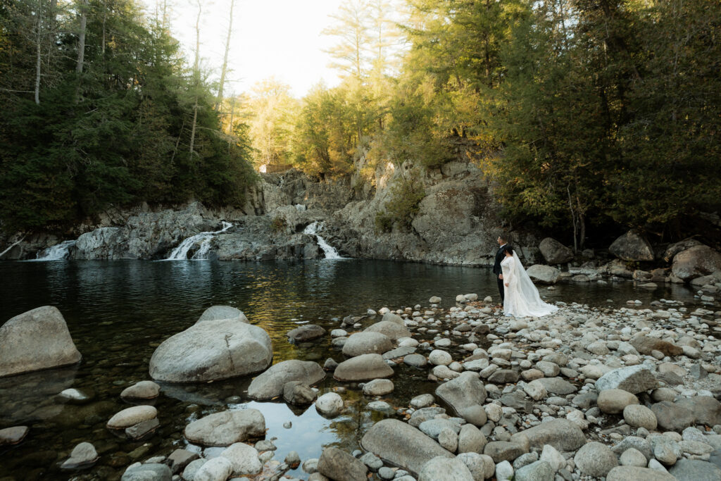 An eloping couple stands at the edge of a waterfall in the Adirondacks.