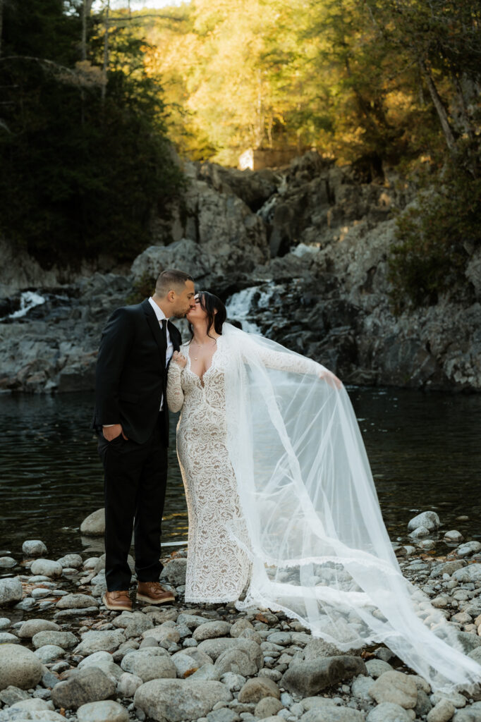 Bride and Groom are at the base of a waterfall in the Adirondacks.