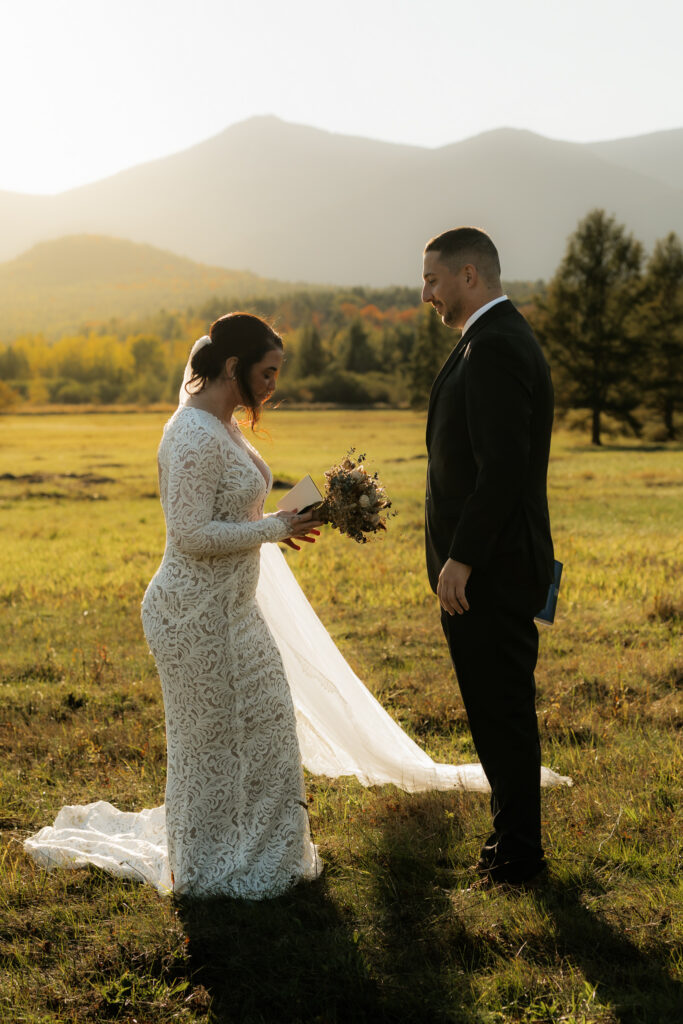 A wilmington ny elopement where a couple is standing in a field exchanging vows at sunset with mountains behind them.