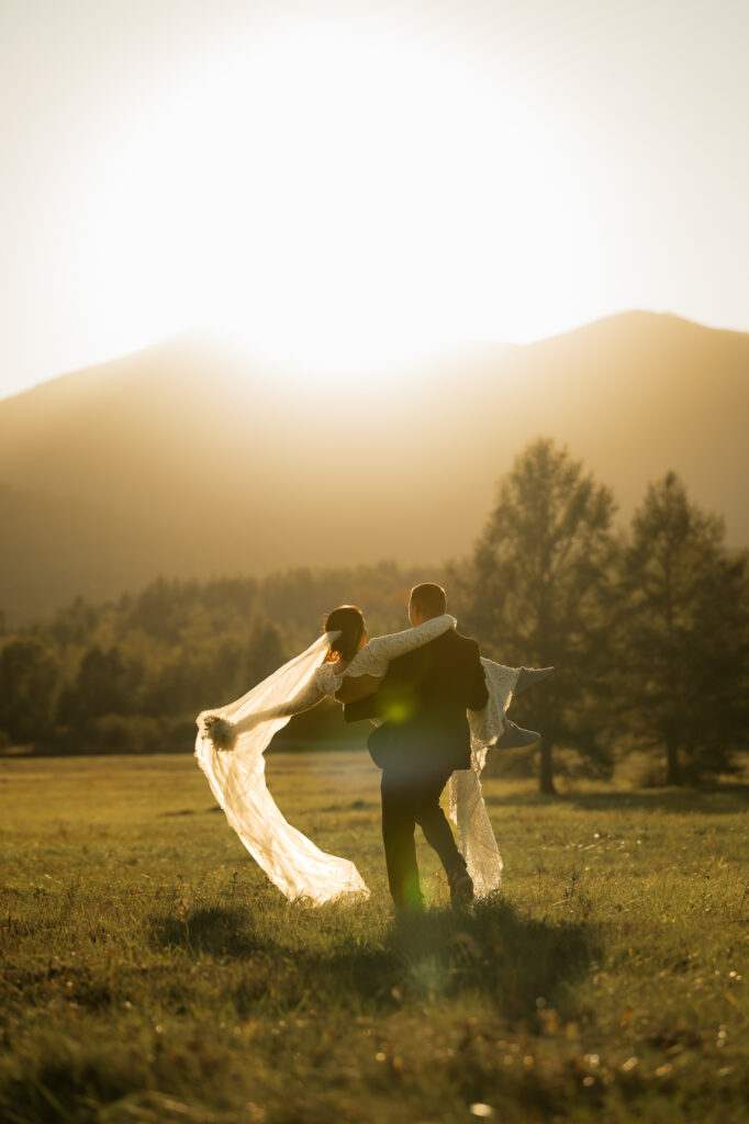 A couple dances in a field at sunset with a mountain backdrop.