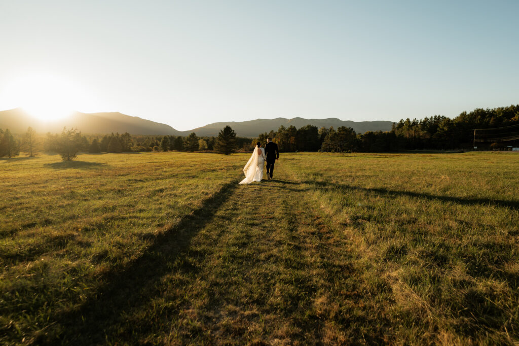 A couple frolics through an Adirondack field at sunset with a mountain backdrop.