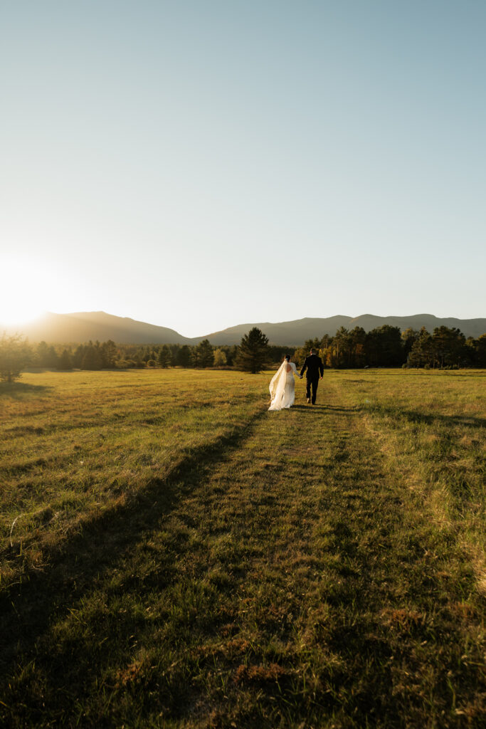 A couple frolics through an Adirondack field at sunset with a mountain backdrop.