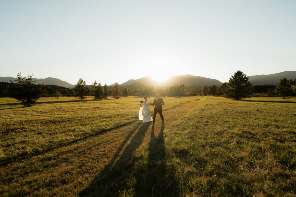 A couple frolics through an Adirondack field at sunset with a mountain backdrop.