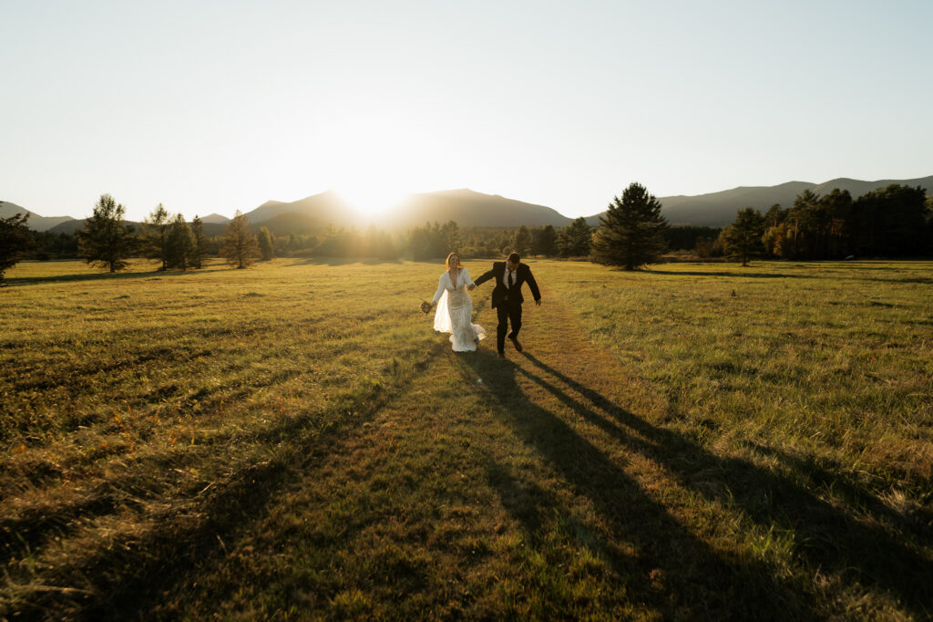 A couple frolics through an Adirondack field at sunset with a mountain backdrop.