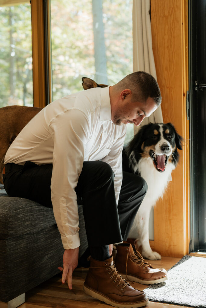 Groom putting wedding shoes on with his dog beside him.
