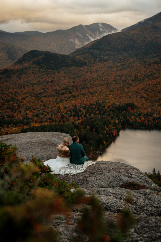 A couple sits and enjoys sunset on a rocky mountain ledge after getting married in Lake Placid New York.